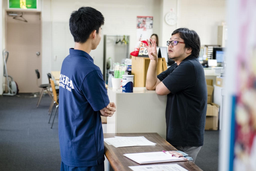 職員室（本館）で教員に質問する学生